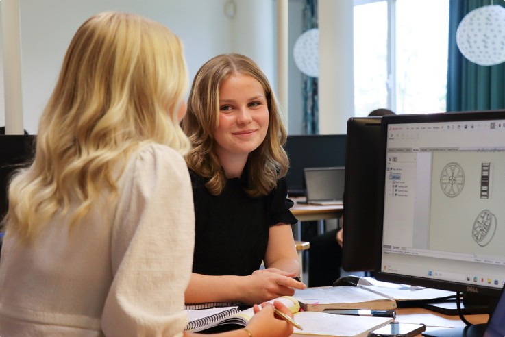 Två kvinnor arbetar tillsammans vid en dator i ett klassrum, med ritningar på skärmen.