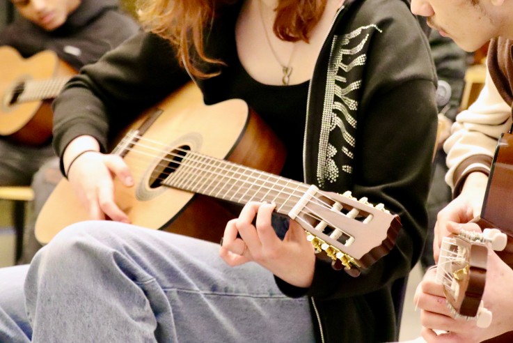 Närbild på personer som spelar akustisk gitarr tillsammans i en grupp.