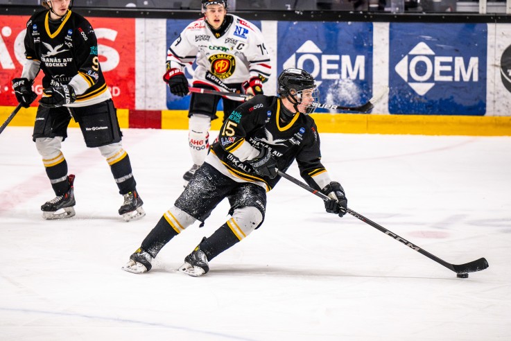 Ishockeyspelare i svart och vitt spelar match på isen, pucken syns vid en klubba.