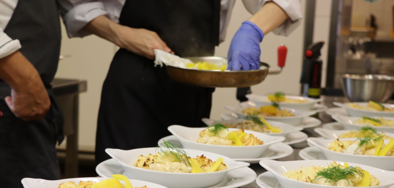 Kockar förbereder flera tallrikar med mat i ett restaurangkök, dekorerar med citron och dill.