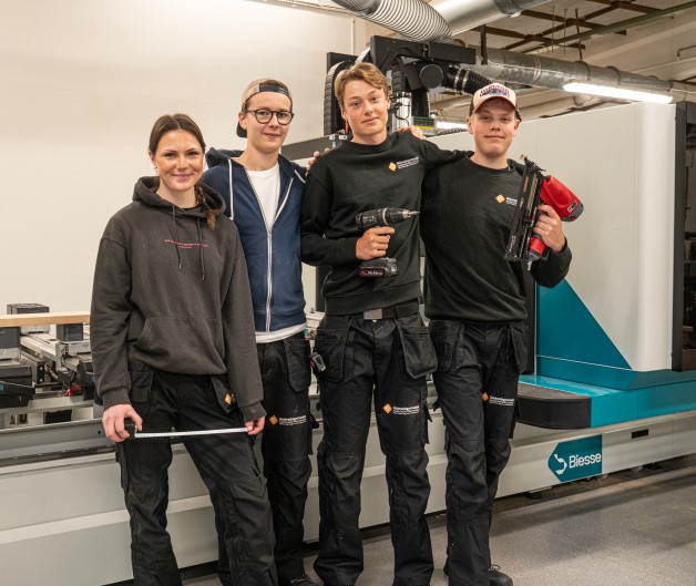 Fyra personer i arbetskläder står framför en stor industrimaskin, tre håller i verktyg.