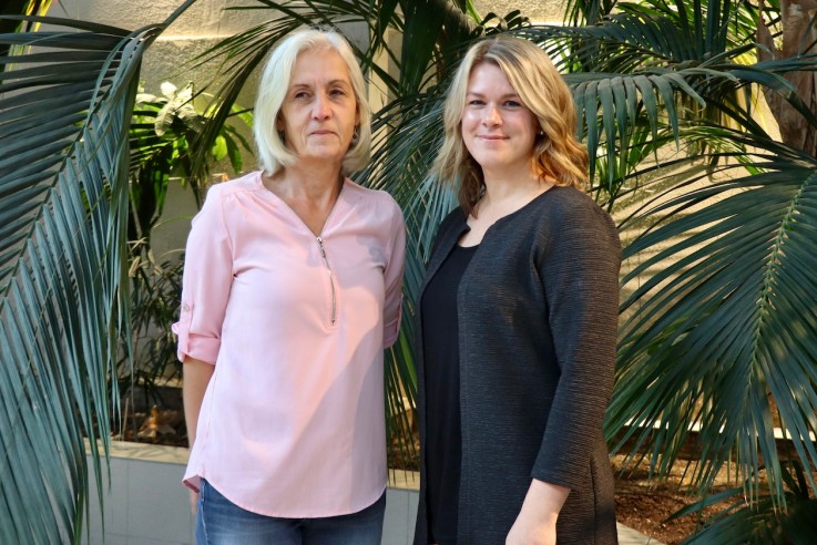 Två kvinnor står bredvid varandra bland stora gröna växter inomhus.