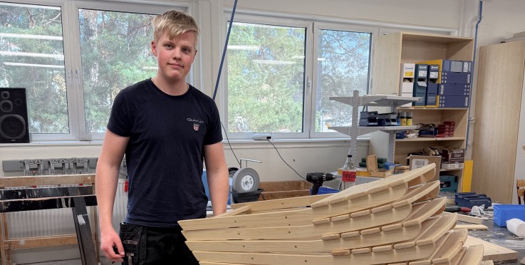 En person står i ett snickeri bredvid en stapel träbitar som ser ut att vara delar till en trappa.