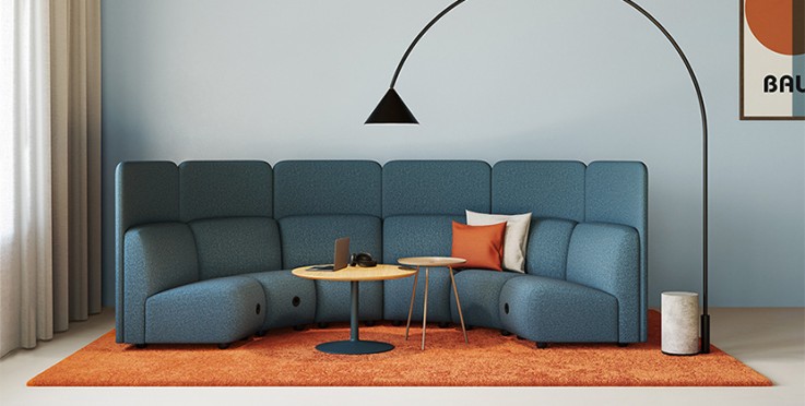 Ett modernt vardagsrum med blå modulsoffa, orange matta, två små bord och en svart golvlampa.