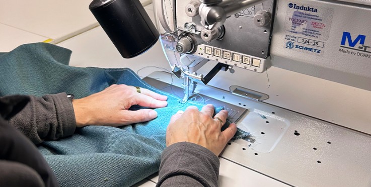 En person syr blått tyg med en industriell symaskin på ett arbetsbord.