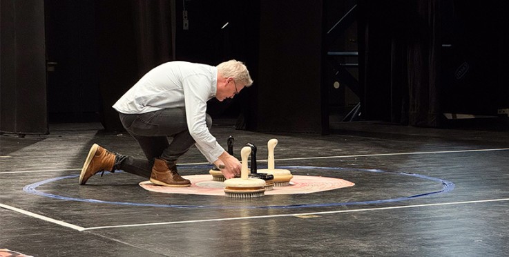En person hukar på en scen och placerar borstar med handtag i en cirkel på golvet.