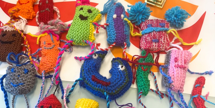 Färgglada virkade figurer med ansikten ligger på ett bord med mönstrad duk och en liten kenyansk flagga.