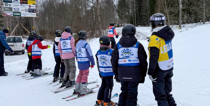 En grupp barn och en ledare står på skidor i snön, redo för skidlektion utomhus.