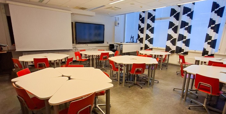 Ett modernt klassrum med vita bord, röda stolar och stora fönster med svartvita gardiner.