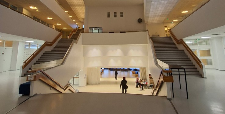 En modern, ljus byggnad med breda trappor och öppna ytor. Några personer går i mitten av bilden.