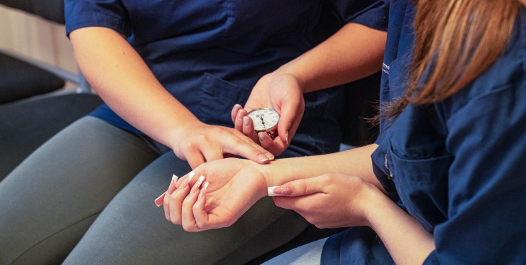 Två personer i blå uniformer mäter puls på handleden med ett tidtagarur.