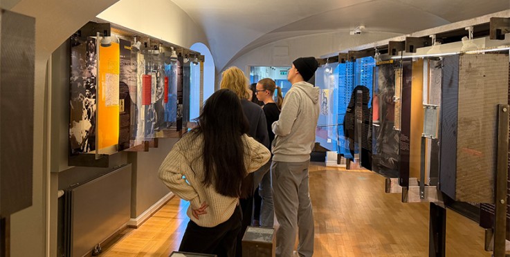 En grupp människor tittar på utställningspaneler i ett museum med trägolv och välvd tak.