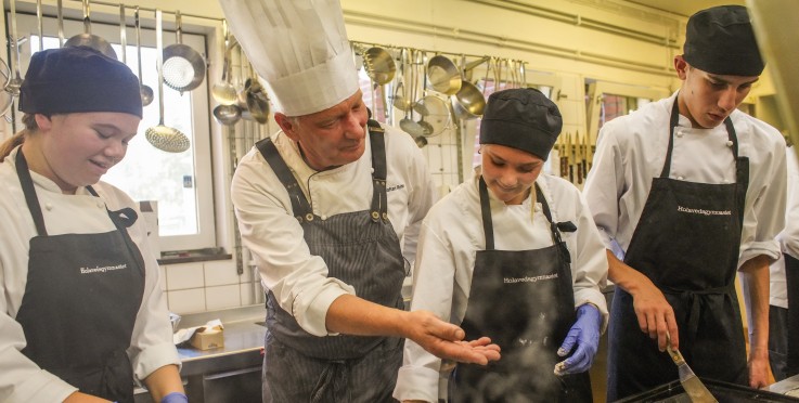 Fyra personer i kockkläder lagar mat tillsammans i ett restaurangkök.