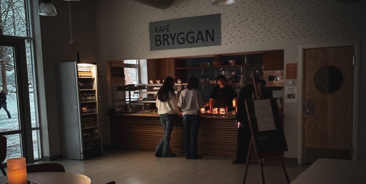 Mörkt kafé med några personer vid disken och tända ljus på ett bord i förgrunden.