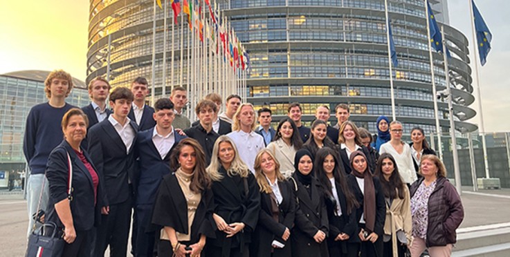 En grupp människor står på trappan framför en modern byggnad med flaggor, troligen ett parlament.