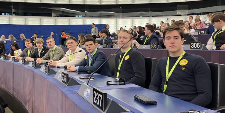 Personer sitter i en stor konferenssal med nummerlappar och mikrofoner framför sig.