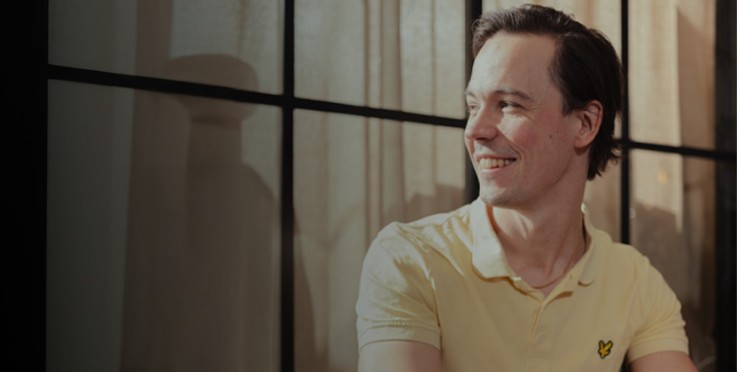 Person i gul pikétröja sitter framför fönster, ansiktet är suddat.