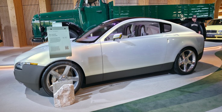 En vit konceptbil står utställd inomhus, med informationsskylt framför och andra bilar i bakgrunden.