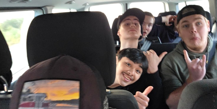 Flera personer sitter i en minibuss, några gör handgester och ansikten är suddade.