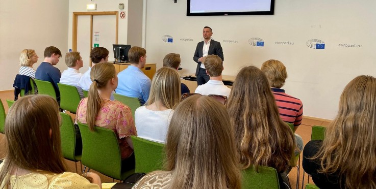 En person håller en presentation inför en grupp sittande åhörare i ett konferensrum.