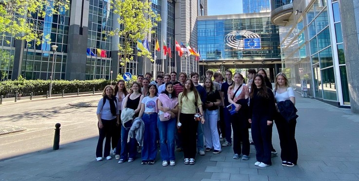 En grupp människor står framför Europaparlamentet i Bryssel, med flaggor och glasbyggnader i bakgrunden.