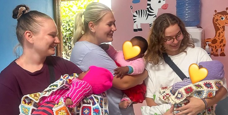 Tre vuxna håller varsin baby i famnen i ett färgglatt rum med djurmålningar på väggen.