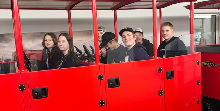 Flera personer sitter i en röd vagn inomhus, ansikten är suddade för anonymitet.