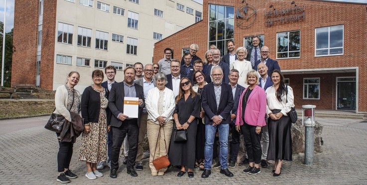 En grupp människor står utanför en tegelbyggnad, poserar för ett gruppfoto.