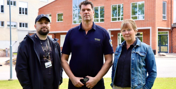 Tre personer står utomhus framför en byggnad, ansikten är suddade för anonymitet.