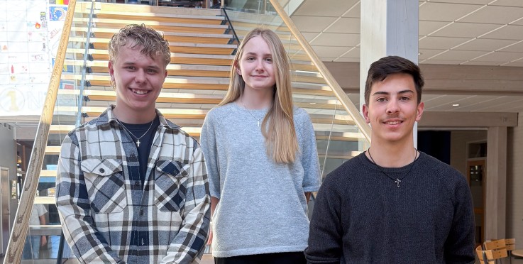 Tre personer står på en trappa inomhus i en ljus och modern byggnad. Deras ansikten är suddade.