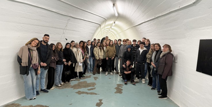 En stor grupp människor står i en vitmålad tunnel med sliten blå golvyta.