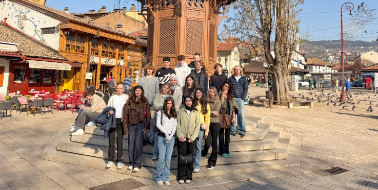 En grupp människor poserar framför Sebilj-fontänen på ett soligt torg i Sarajevo.