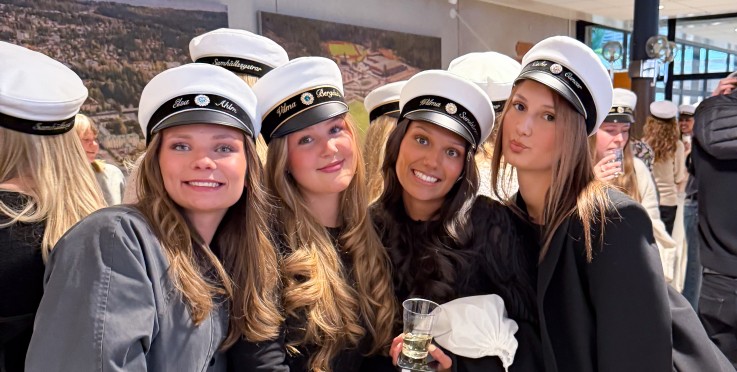 En grupp unga kvinnor i studentmössor poserar tillsammans inomhus, klädda i svart och vitt.