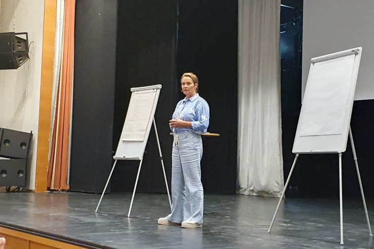 En kvinna står på en scen och håller en presentation inför en liten publik, med två blädderblock bredvid sig.