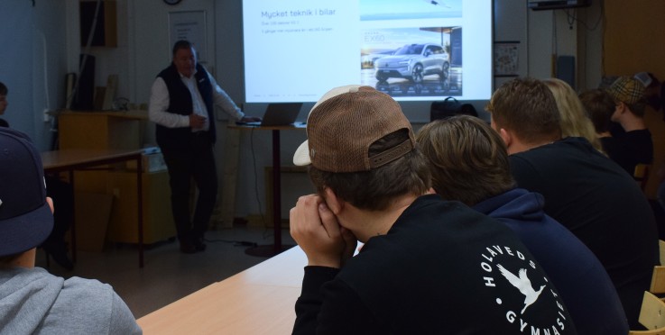 En grupp elever sitter i ett klassrum och lyssnar på en föreläsare som visar en presentation om teknik i bilar.